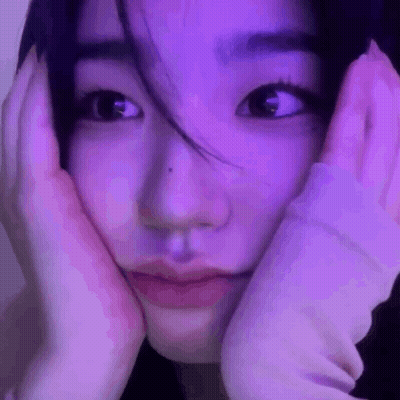 A Close Up Of A Woman 'S Face With Her Hands On Her Face In Front Of A Purple Light . GIF