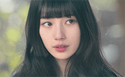 A Close Up Of A Woman 'S Face With Long Black Hair And Bangs Looking At The Camera . GIF