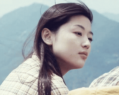 A Close Up Of A Woman 'S Face With Mountains In The Background GIF
