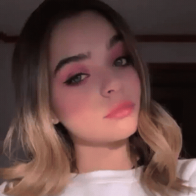 A Close Up Of A Woman 'S Face With Pink Eye Shadow And A White Shirt . GIF
