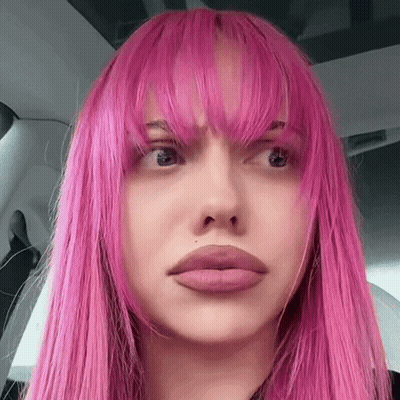 A Close Up Of A Woman 'S Face With Pink Hair And Bangs GIF