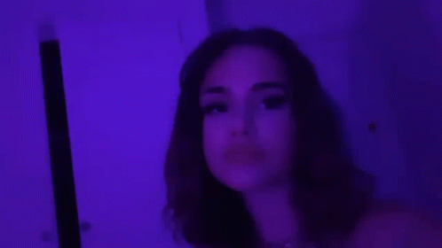 A Close Up Of A Woman 'S Face With Purple Lights Behind Her . GIF