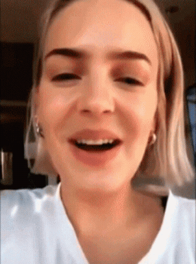 A Close Up Of A Woman 'S Face With Short Blonde Hair And A White Shirt Smiling . GIF