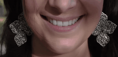 A Close Up Of A Woman 'S Mouth Wearing Earrings And Smiling GIF