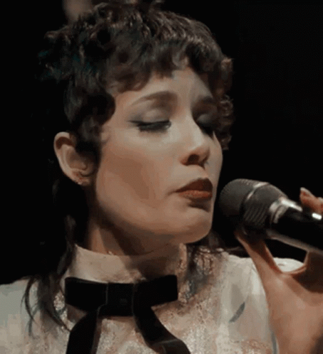 A Close Up Of A Woman Singing Into A Microphone With Her Eyes Closed GIF