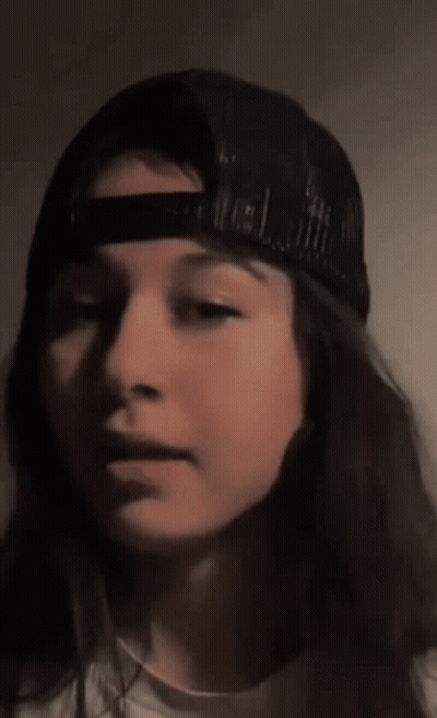 A Close Up Of A Woman Wearing A Baseball Cap Covering Her Mouth With Her Hand . GIF