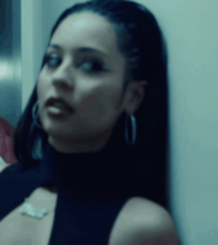 A Close Up Of A Woman Wearing A Black Top And Earrings GIF