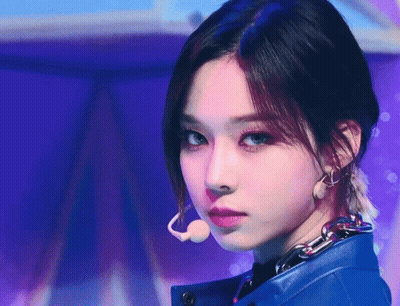 A Close Up Of A Woman Wearing A Blue Jacket And Earrings GIF