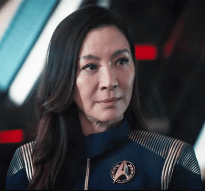 A Close Up Of A Woman Wearing A Blue Jacket With A Star Trek Emblem On It . GIF