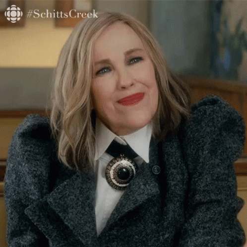 A Close Up Of A Woman Wearing A Coat And Tie With The Word Schitts Creek In The Corner GIF