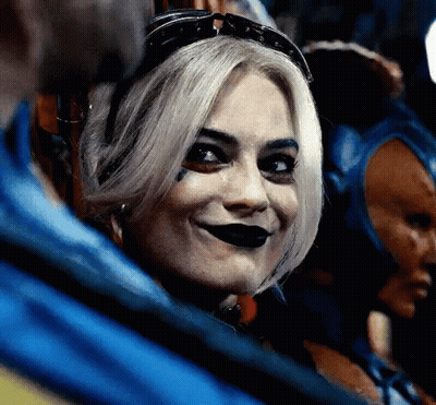 A Close Up Of A Woman Wearing A Harley Quinn Costume And Sunglasses Smiling . GIF