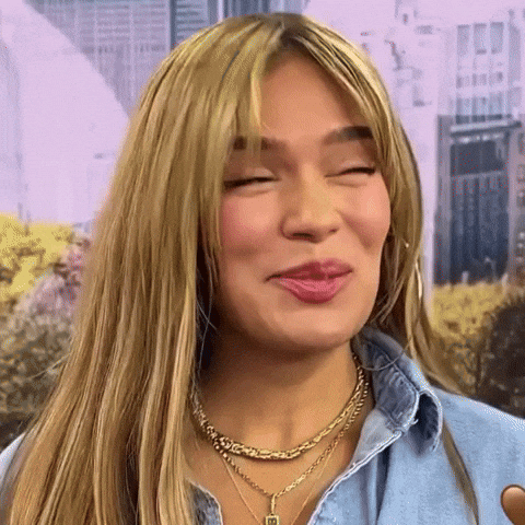 A Close Up Of A Woman Wearing A Necklace And A Denim Shirt Making A Funny Face . GIF