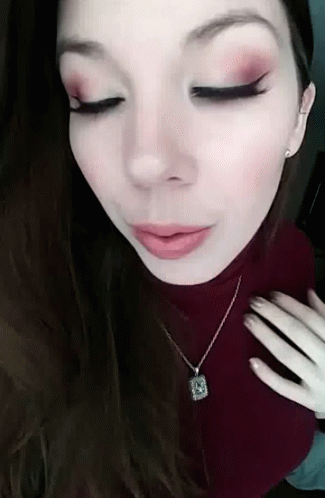 A Close Up Of A Woman Wearing A Necklace And A Red Turtleneck Sweater . GIF