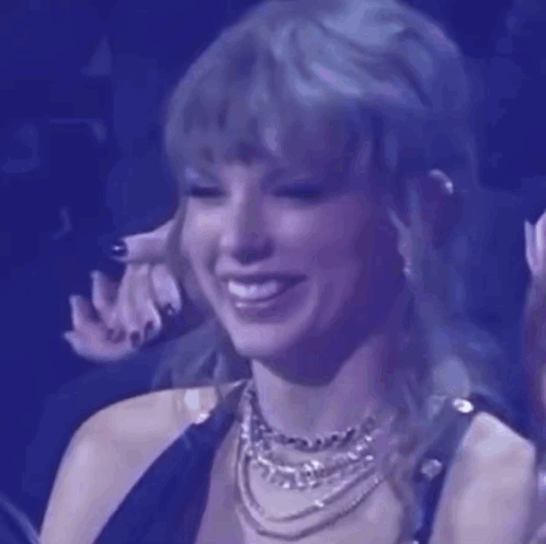 A Close Up Of A Woman Wearing A Necklace And Smiling At A Concert . GIF