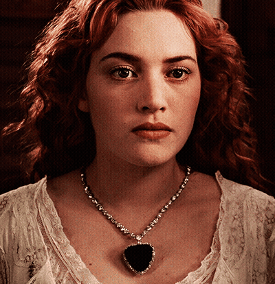 A Close Up Of A Woman Wearing A Necklace With A Heart Shaped Pendant GIF