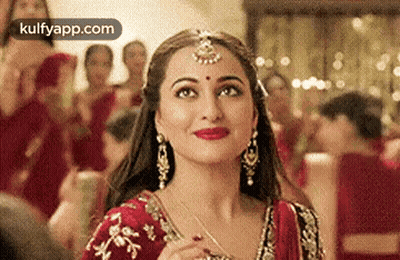 A Close Up Of A Woman Wearing A Red And Gold Dress And Earrings . GIF