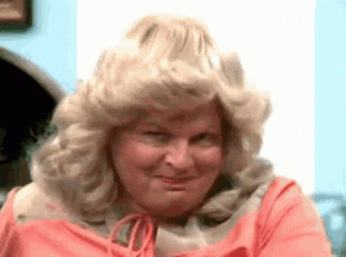 A Close Up Of A Woman Wearing A Wig And A Pink Shirt . GIF