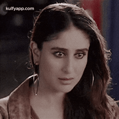 A Close Up Of A Woman Wearing Earrings And A Brown Jacket Looking At The Camera . GIF