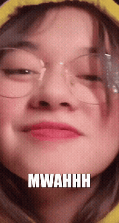 A Close Up Of A Woman Wearing Glasses And A Yellow Hoodie With The Words Mwahhh Written On Her Face . GIF
