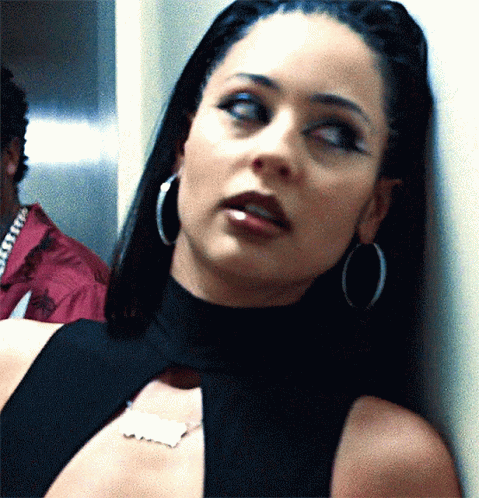 A Close Up Of A Woman Wearing Hoop Earrings And A Name Tag On Her Neck GIF
