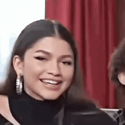 A Close Up Of A Woman Wearing Hoop Earrings Smiling And Looking At The Camera . GIF