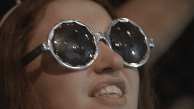 A Close Up Of A Woman Wearing Sunglasses With A Reflection Of A Person 'S Face In Them GIF