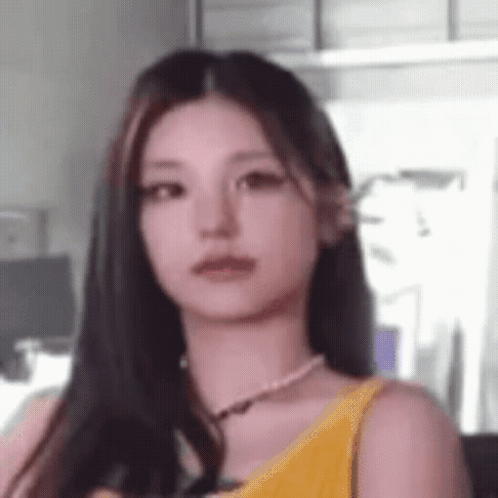A Close Up Of A Woman With Long Hair Wearing A Yellow Tank Top And A Pearl Necklace . GIF