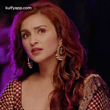 A Close Up Of A Woman With Red Hair Wearing Earrings And A Red Top . GIF