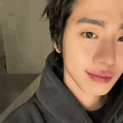 A Close Up Of A Young Man 'S Face Wearing A Black Hoodie And Smiling . GIF