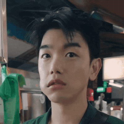 A Close Up Of A Young Man 'S Face With A Green Bag Hanging On The Wall Behind Him GIF