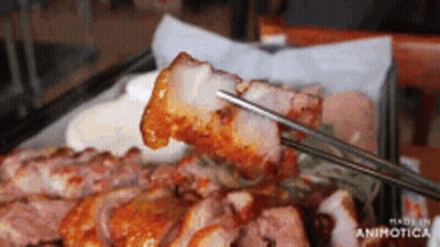 A Close Up Of Chopsticks Holding A Piece Of Meat Over A Plate Of Meat GIF
