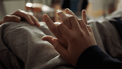 A Close Up Of Two People Holding Hands On A Bed GIF