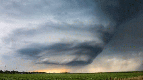 A Cloudy Sky Over A Field With A Few Trees In The Distance GIF