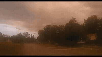 A Cloudy Sky With A Few Trees In The Foreground And A Few Houses In The Background GIF