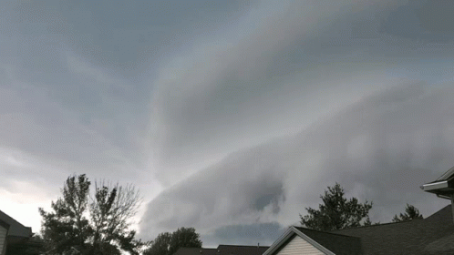 A Cloudy Sky With A House In The Foreground And Trees In The Background GIF