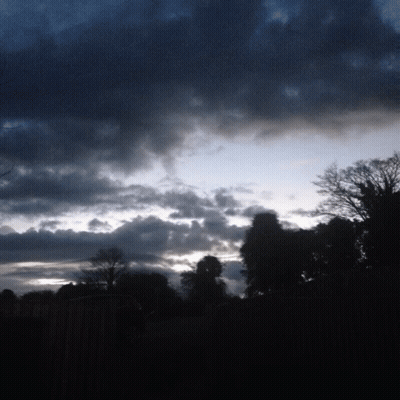 A Cloudy Sky With Trees In The Foreground And A Fence In The Background GIF
