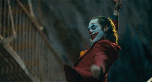 A Clown In A Red Suit And Yellow Vest Is Waving GIF
