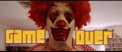A Clown In A Red Wig Is Standing In Front Of A Game Over Sign GIF