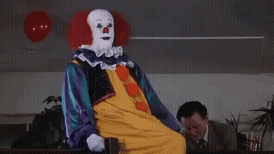 A Clown Is Sitting In A Chair In Front Of A Man In A Suit . GIF