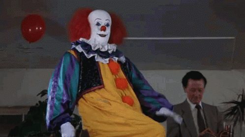 A Clown Is Sitting In Front Of A Man In A Suit . GIF
