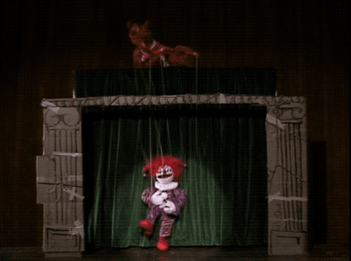 A Clown Puppet Is Being Held Up By A String On A Stage GIF