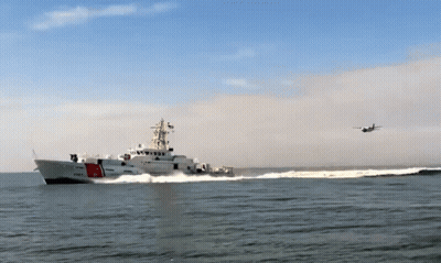 A Coast Guard Ship With A Plane Flying Overhead GIF