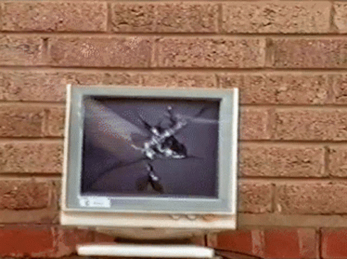 A Computer Monitor With A Broken Screen Is Sitting On A Table In Front Of A Brick Wall GIF