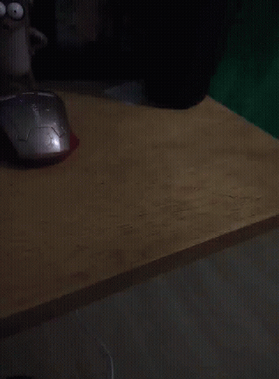A Computer Mouse Sits On A Wooden Desk Next To A Cartoon Character GIF