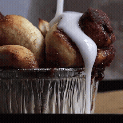 A Container Of Cinnamon Rolls With Icing On Top GIF