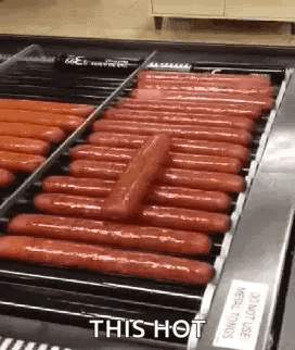 A Conveyor Belt Filled With Hot Dogs Is Being Cooked . GIF