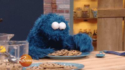 A Cookie Monster Is Sitting At A Table With A Plate Of Chocolate Chip Cookies GIF