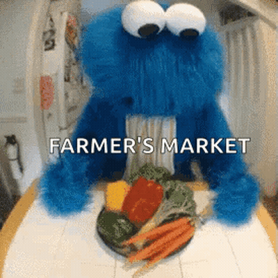 A Cookie Monster Is Sitting At A Table With A Plate Of Vegetables And The Words " Farmer 'S Market " Above It GIF