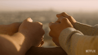 A Couple Holding Hands With A Netflix Logo Behind Them GIF