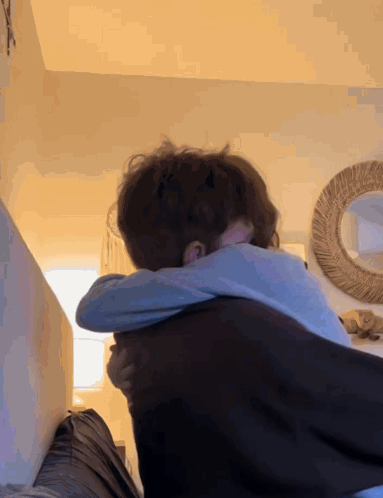 A Couple Hugging Each Other In A Room With A Mirror In The Background GIF